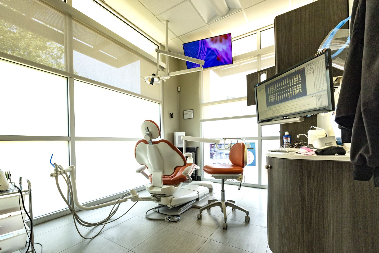 Sunlit treatment room with floor-to-ceiling windows and a ceiling-mounted TV